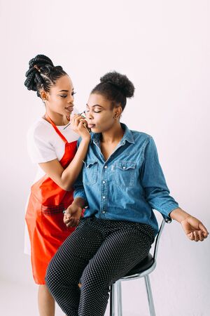 Young beautiful African American woman applying professional make-up by African make-up artist. Studio shootの写真素材
