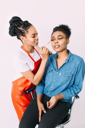 Young beautiful African American woman applying professional make-up by African make-up artist. Studio shootの写真素材