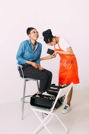 Young beautiful African American woman applying professional make-up by African make-up artist. Studio shootの写真素材