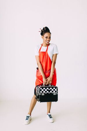 Beautiful young African American beautician woman holding set of makeup equipment in special case, isolated on white backgroundの写真素材