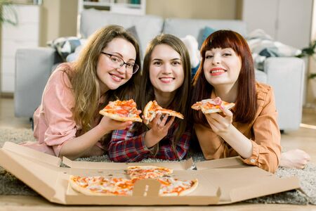 friendship, people, home party and food concept - close up of three pretty happy women friends or girls eating pizza at homeの写真素材