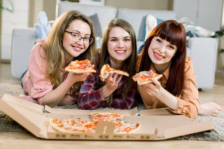 friendship, people, home party and food concept - close up of three pretty happy women friends or girls eating pizza at homeの写真素材