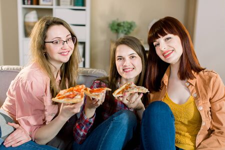 Pizza time. Three pretty smiling women eating pizza, having fun together in the home dining room. Frienship, food, lifestyle conceptの写真素材