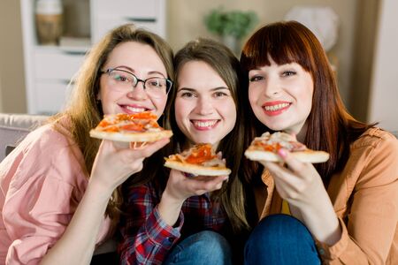 Closeup photo of three cheerful smiling girls celebrating a party at home and eating pizza.の写真素材