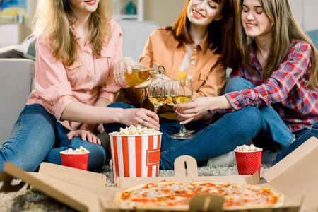 young Caucasian women sitting indoor, eating pizza and popcorn and drinking together â friendship, cheerful, celebrationの写真素材