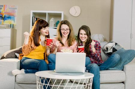 Happy young girls or football fans eating popcorn while watching soccer on laptop and celebrating...