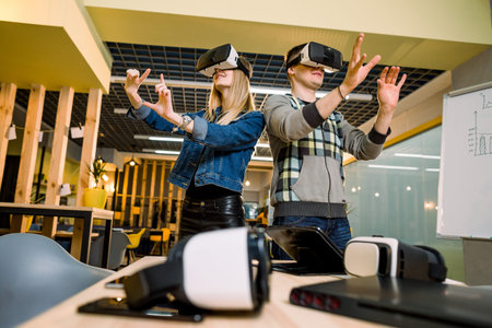 amazed young beautiful couple testing virtual reality 3D video glasses VR headset dressed in casual...