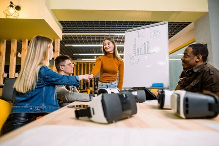 Multiethnical business people having team training exercise during seminar with VR glasses. Young girl in orange sweater presenting results of the project for coworkersの写真素材
