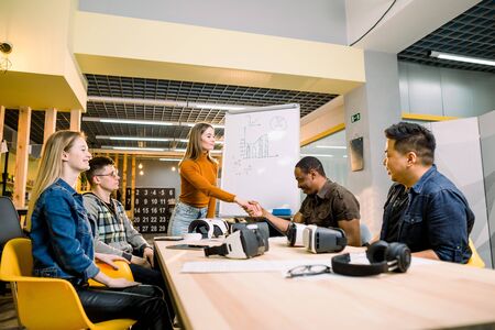Business team in casual wear having meeting about new project of virtual reality simulator. Young woman in casual wear shaking hands with colleagues in the modern loft officeの写真素材