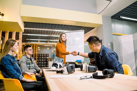 Business team in casual wear having meeting about new project of virtual reality simulator. Young woman in casual wear shaking hands with colleagues in the modern loft officeの写真素材
