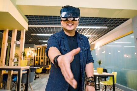 Young Chinese businessman working in office with virtual reality glasses on head. Man using VR headset for handshaking in augmented realityの写真素材