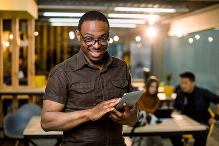 young creative African man in modern office. Group of young Multiracial people are working together with laptop, tablet, smart phone, notebook. Successful hipster team in coworking. Freelancers.の写真素材