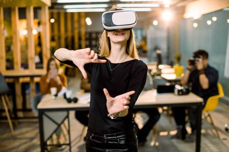 Woman in VR headset touching objects in virtual reality. Girl interacting with 3d visualization. Modern IT product test on digital simulator concept. Team of IT workers on the backgroundの写真素材