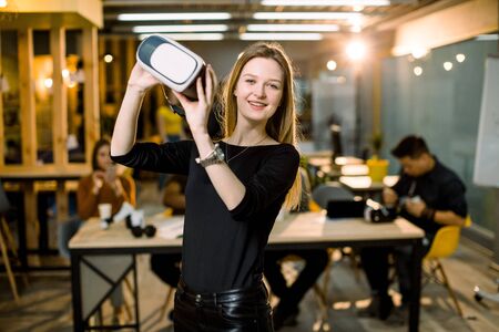 The beautiful girl posing with virtual reality goggles at the office. Coworkers team at the table on the backgroundの写真素材