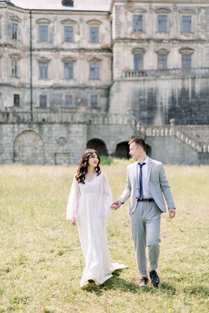 Happy wedding couple standing and walking near old ancient castleの写真素材