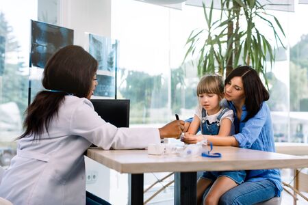 medicine, healthcare and pediatry concept - african american doctor giving treatment recommendations for caucasian mother with baby daughter at modern clinicの写真素材