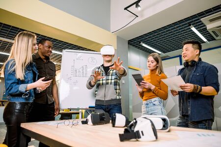 Multiethnic Business team presenting virtual reality headset in office meeting for young handsome man chief. Developers meeting with virtual reality simulator around table in creative office.の写真素材