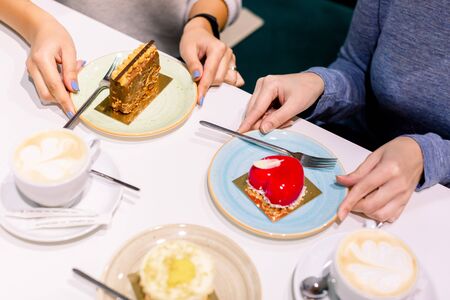 Drinking coffee and eating desserts together. Top view of hands of two beautiful women keeping hands on plates with delicious desserts in cafe. Meeting of best friend. Coffee with cakesの写真素材