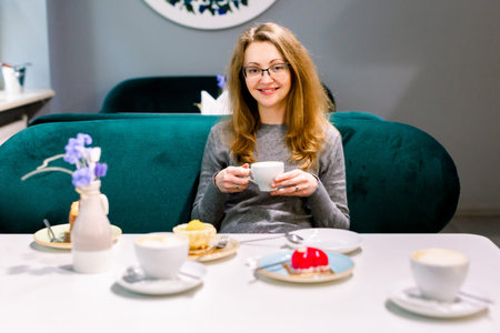 beautiful young woman sitting and drinking coffee or tea. Closeup of pretty blond young woman...