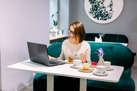 Freelance woman working with laptop in a cafe. Young beautiful serious woman with short dark hair in glasses works on laptop in cafe. Confident young woman in smart casual wear working on laptopの写真素材