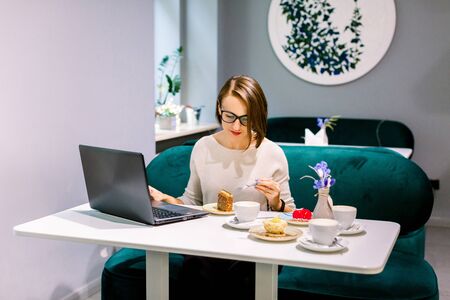 Soft focus shot of woman at coworking space or cafe with internet connection, work on laptop and enjoy desserts, waiting for clients. Concentrated at work.の写真素材