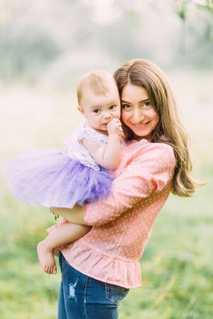 Young mother holding daughter in her arms. Beautiful Mother And Baby outdoors. Nature. Beauty Mum and her Child playing in Park together. Outdoor Portrait of happy family. Joy. Mom and Babyの写真素材