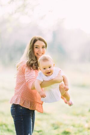 Young mother holding daughter in her arms. Beautiful Mother And Baby outdoors. Nature. Beauty Mum and her Child playing in Park together. Outdoor Portrait of happy family. Joy. Mom and Babyの写真素材