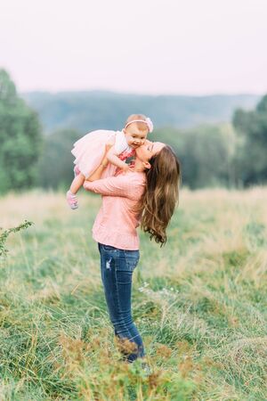 Mother and little daughter playing together in a park. Happy cheerful family. Mother and baby kissing, laughing and hugging in nature outdoorsの写真素材