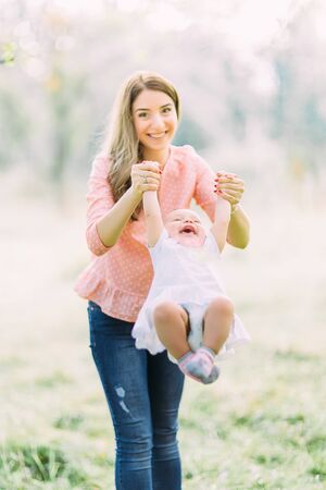 Young mother holding daughter in her arms. Beautiful Mother And Baby outdoors. Nature. Beauty Mum and her Child playing in Park together. Outdoor Portrait of happy family. Joy. Mom and Babyの写真素材