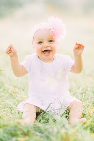 Portrait of happy joyful child in white dress over green grass background. Happy little baby girl in the park. Family conceptの写真素材