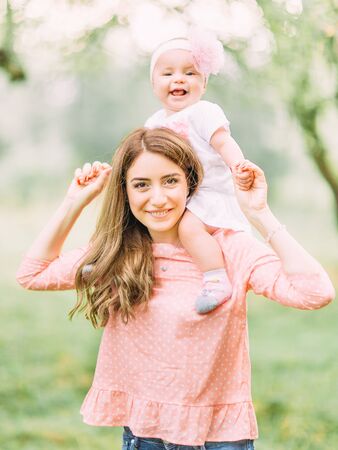 Mother and little daughter playing together in a park. Happy cheerful family. Mother and baby kissing, laughing and hugging in nature outdoorsの写真素材