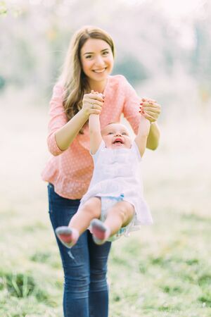 Young mother holding daughter in her arms. Beautiful Mother And Baby outdoors. Nature. Beauty Mum and her Child playing in Park together. Outdoor Portrait of happy family. Joy. Mom and Babyの写真素材