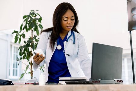 Black female doctor at work in an office, looking to laptop. Beautiful African American woman doctor or nurse working on a laptop computer in modern clinicの写真素材