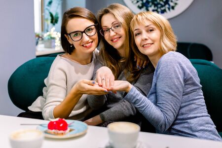 Beautiful fiancee. Nice happy woman posing for a photo while showing her engagement ring together with her two women freinds in cafe indoorsの写真素材
