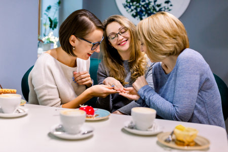 Looking at ring. Blonde-haired and dark-haired women holding hand of their pretty friend looking at...