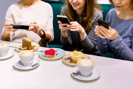 Women friends looking at cakes in cafe, making photos on the smartphones. Friends looking at photographs and laughing, cafe women, fun, enjoyingの写真素材
