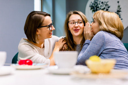Gossips with best friends. Horizontal shot of two beautiful women whispering to their third friends...