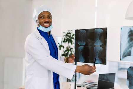 Medical office and doctor practice concept. Professional smiling african american doctor at clinic pointing on X-ray.の写真素材