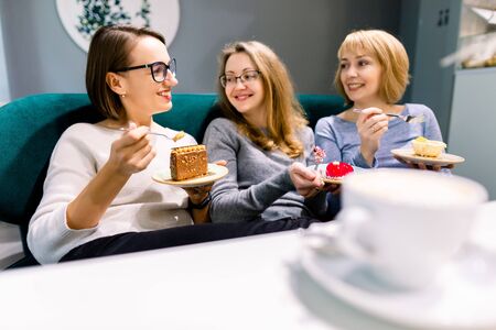 Meeting with best friend. Horizontal shot of beautiful three women talking while drinking coffee with desserts in vintage cafe. Women friends gossiping during coffee time.の写真素材