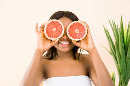 Beauty african woman with orange citrus grapefruit cover eyes with healthy skin body, isolated over white background. Attractive fresh vitamin. Studio shotの写真素材
