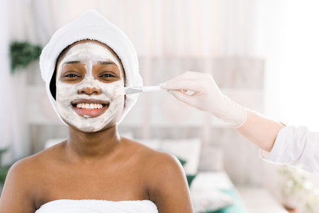 Young African woman in Studio doing body care with refreshing facial mask for young and beautiful...