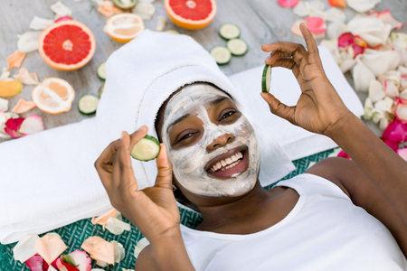 Beauty treatment. Top view of beautiful young African woman lying with pieces of cucumber on her...