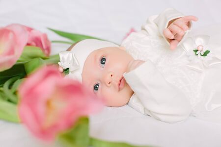 A little beautiful newborn girl in a white dress is lying on the bed among the flowersの写真素材