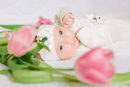 A little beautiful newborn girl in a white dress is lying on the bed among the flowersの写真素材
