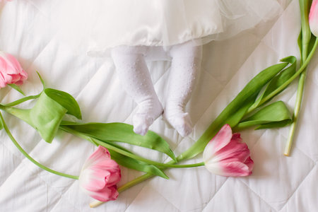 A little beautiful newborn girl in a white dress is lying on the bed among the flowersの写真素材