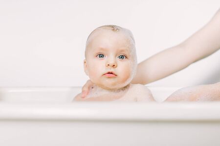 Happy laughing baby taking a bath playing with foam bubbles. Little child in a bathtub. Infant washing and bathingの写真素材