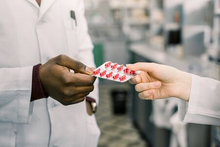 Male And Female Pharmacists or doctors In Pharmacy. Welcome in drugstore. Cropped image of hands of pharmacists or doctors holding blister of red capsulesの写真素材