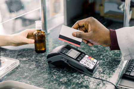 Cropped image of hands of African Man pharmacist holding credit card of client and hand of woman...