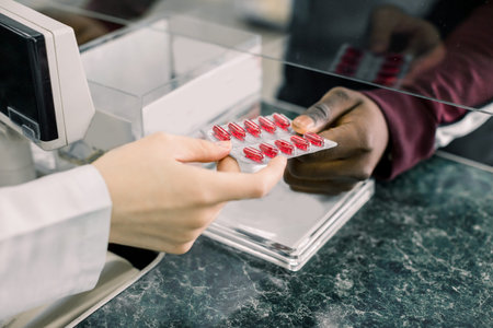 Cropped image of hands of woman pharmacist giving red pills to black man in drugstoreの写真素材