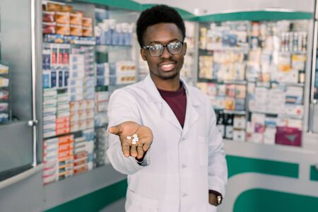 African-american doctor pharmacist man holding and offering white pills. Drug store and drug quality conceptの写真素材